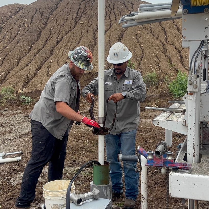 Two TR Drilling crew members servicing a wellhead in the field