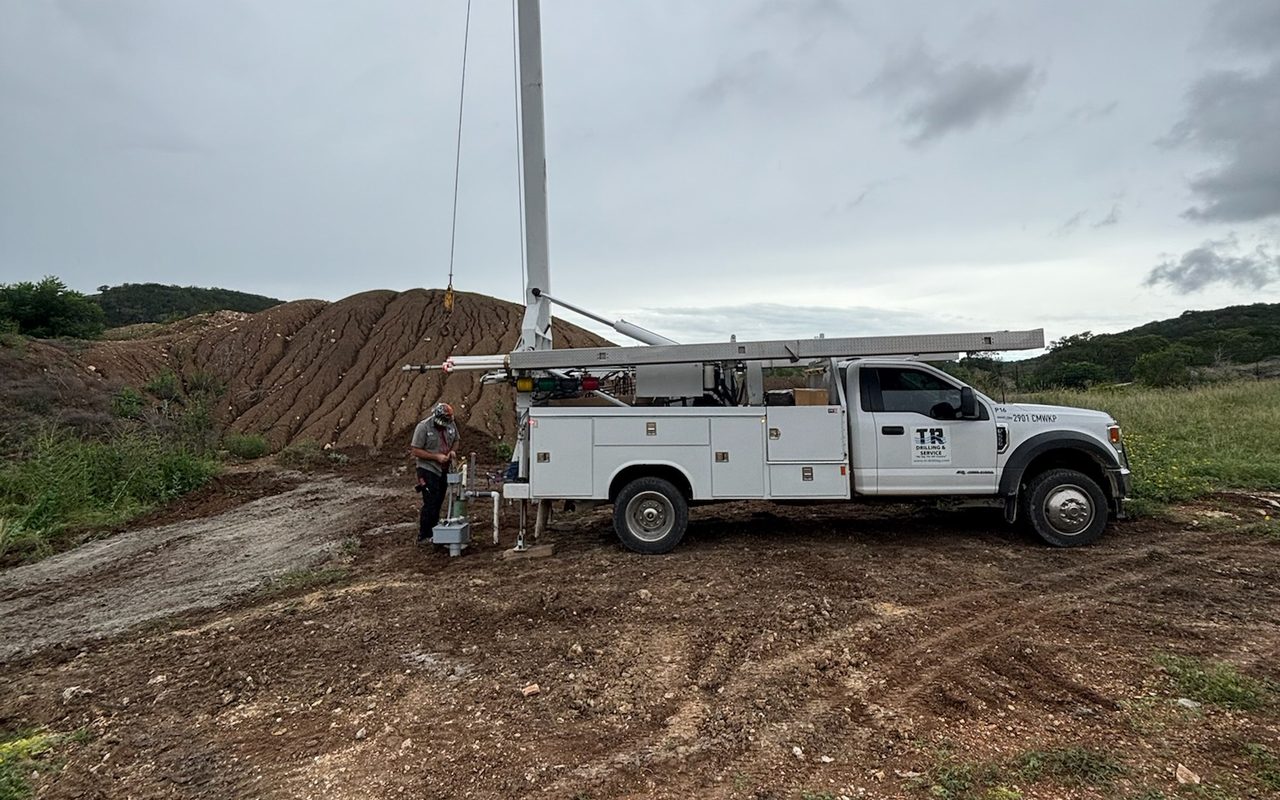 A TR Drilling crew member servicing a well pump in the field with the truck-mounted hoist, in the Texas Hill Country